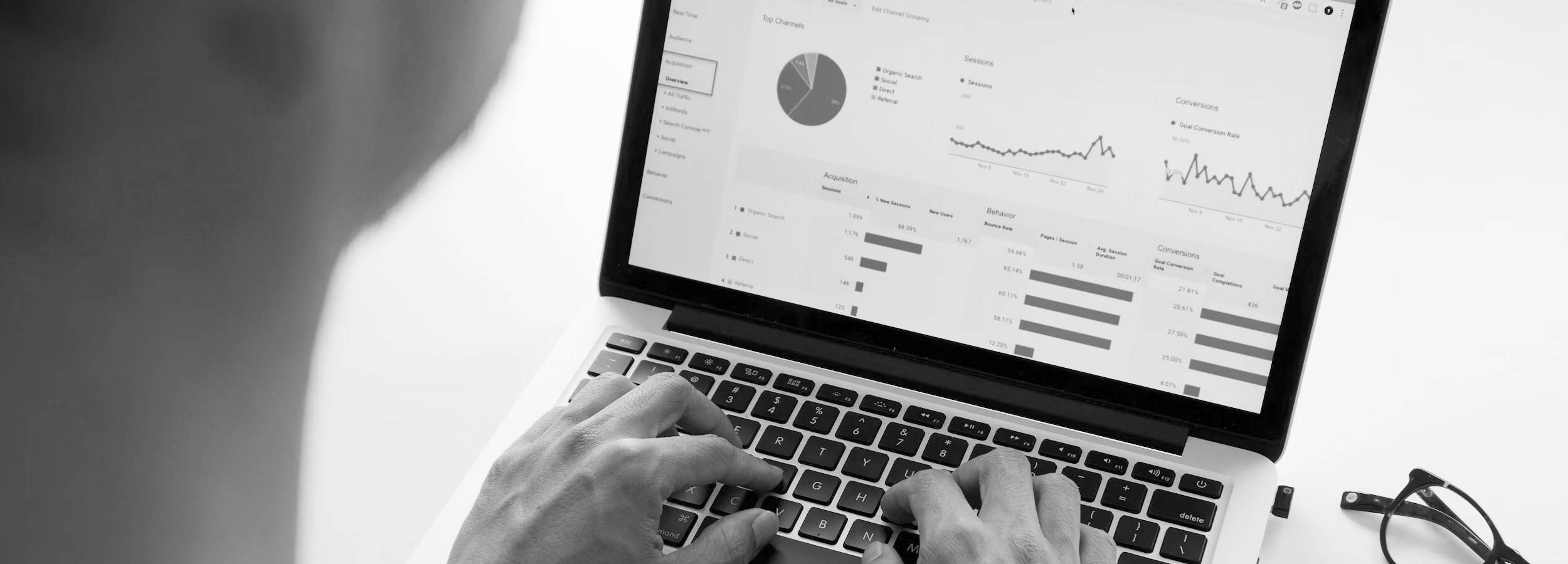 A black and White image of someones hands on a laptop with Analytical data on the screen